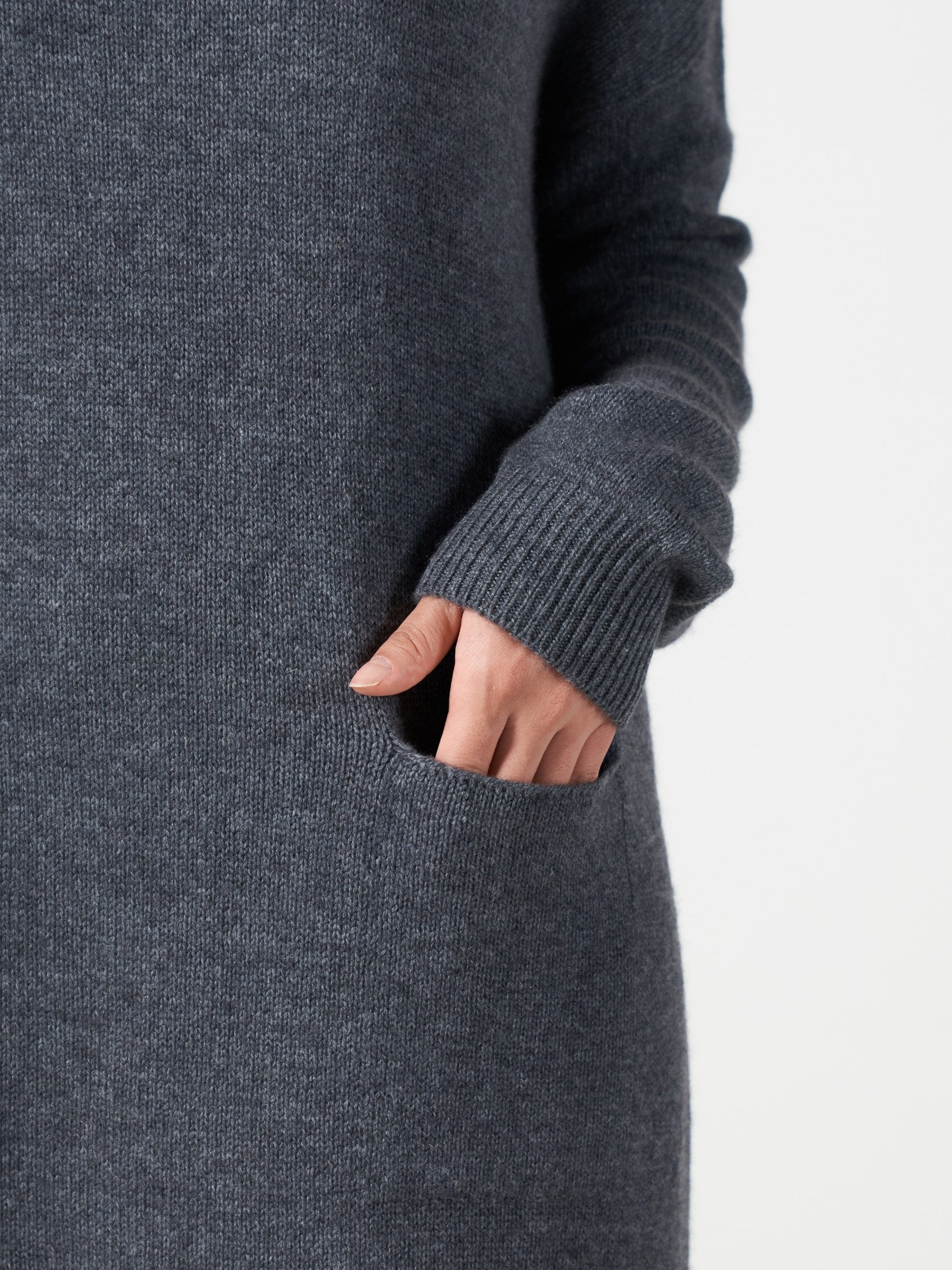 Close-up of a grey cashmere dress with a single pocket and ribbed cuff on the sleeve, showing a hand inside the pocket
