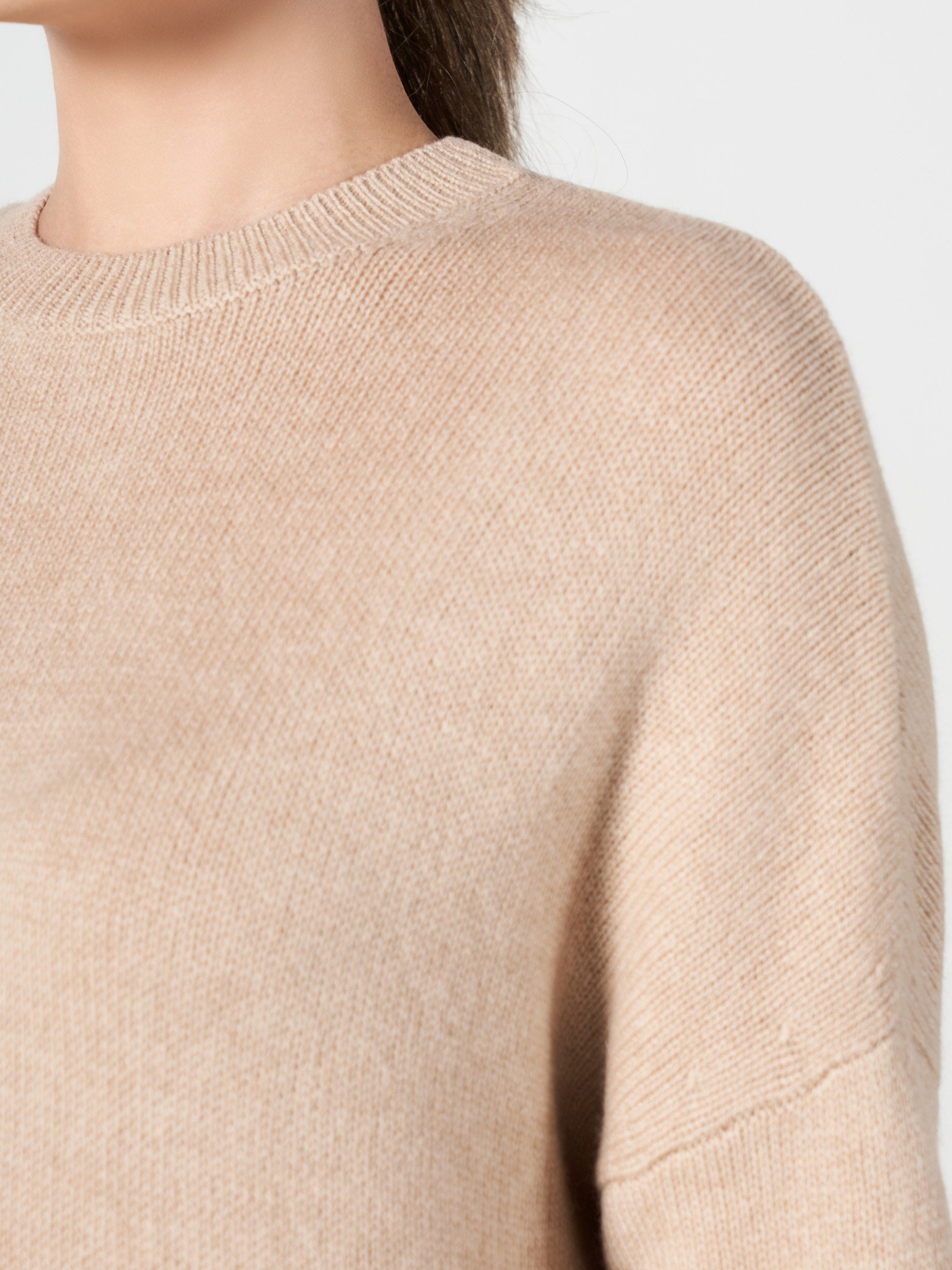 Close-up of beige cashmere one pocket loose dress showing soft knit texture and round neckline on a woman.
