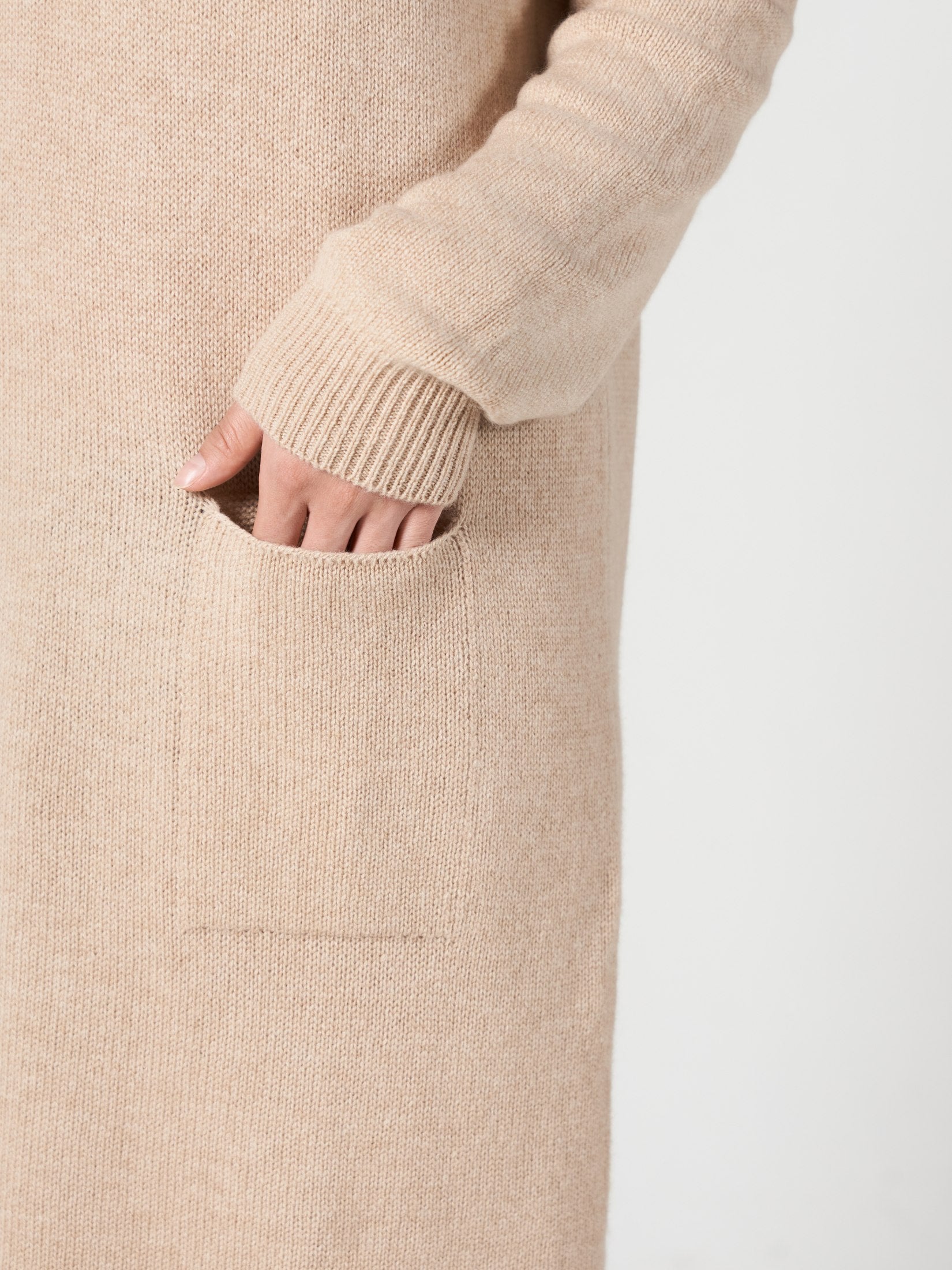 Close-up of a hand in the one pocket of a beige cashmere loose fit dress sleeve visible