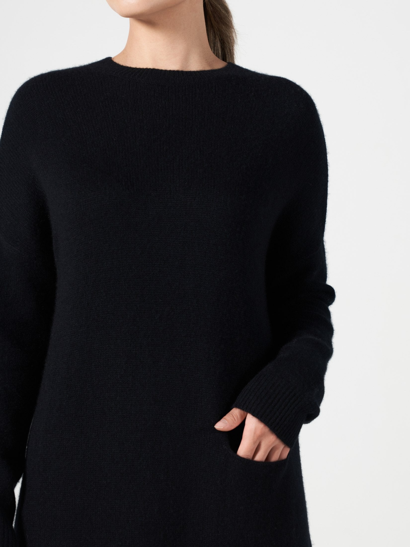 Woman wearing a black loose fit cashmere dress with a round neck and one pocket, minimalist and elegant design.