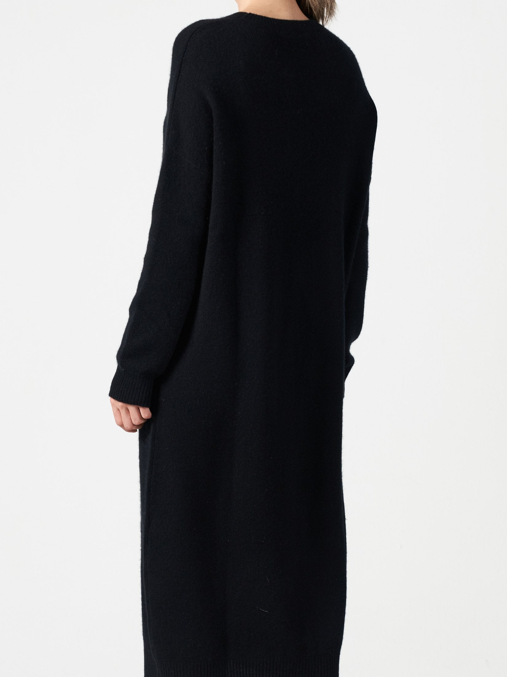 Woman wearing a black relaxed fit cashmere dress with long sleeves and a round neck, shown from the back