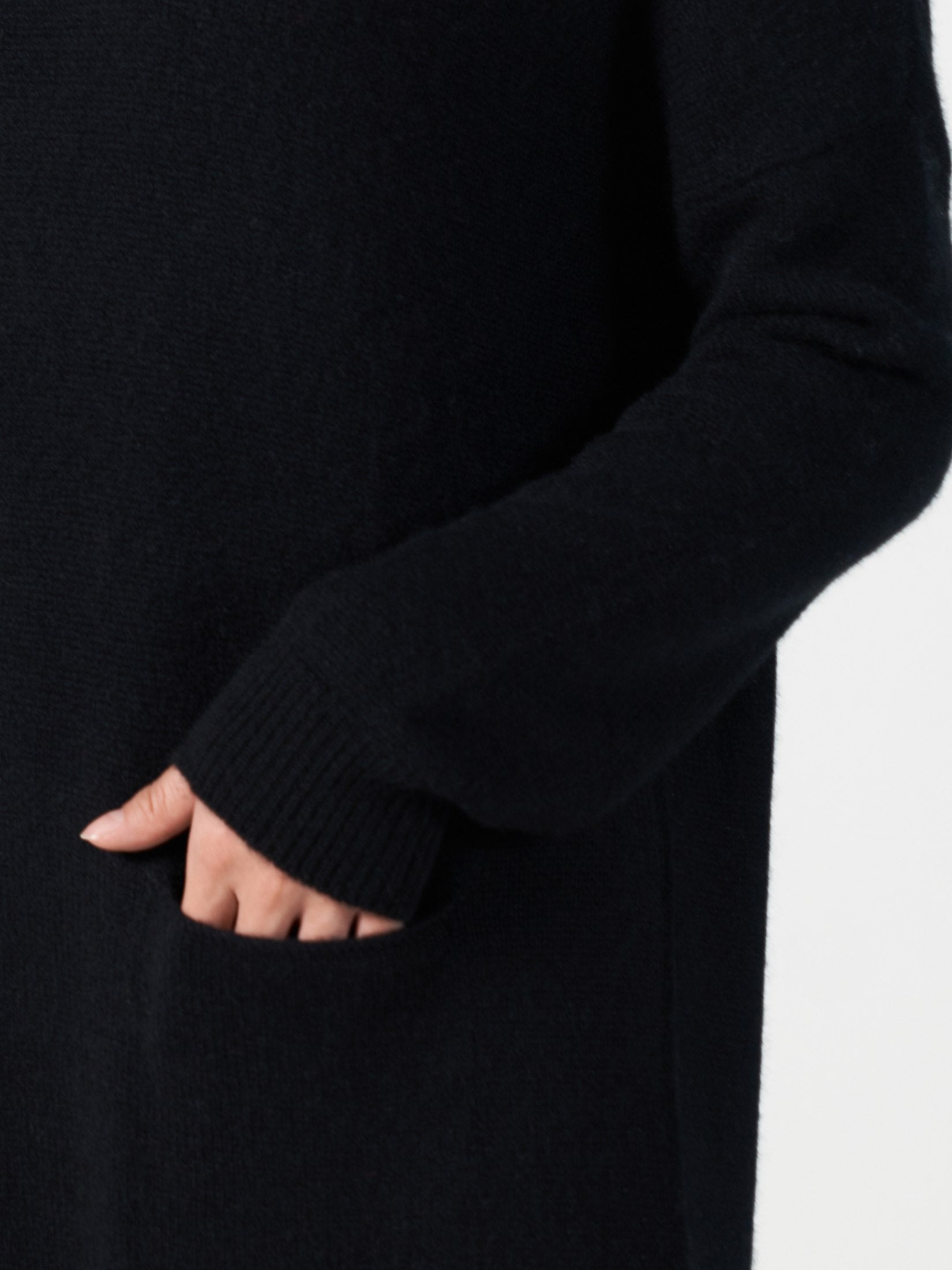 Close-up of a black cashmere dress sleeve and hand inside the dress's single front pocket showing soft knit texture.