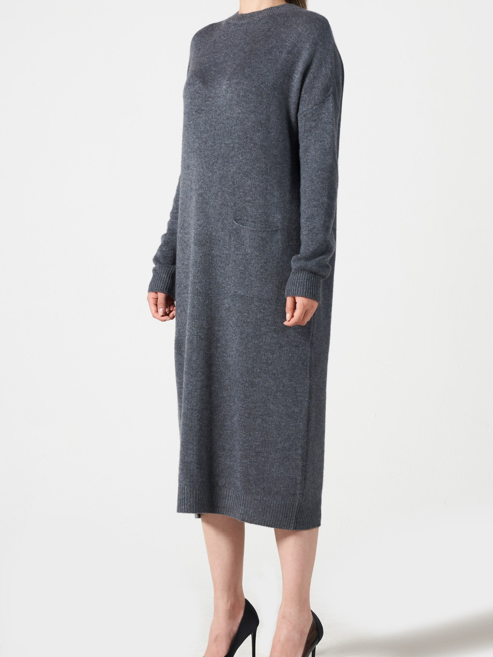 Woman wearing a relaxed fit grey cashmere dress with long sleeves and one pocket, paired with black heels