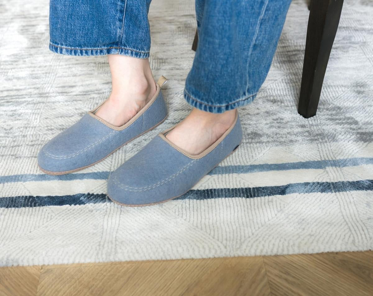 Light blue felt slip-on slippers worn, highlighting their soft material and comfortable, casual design.