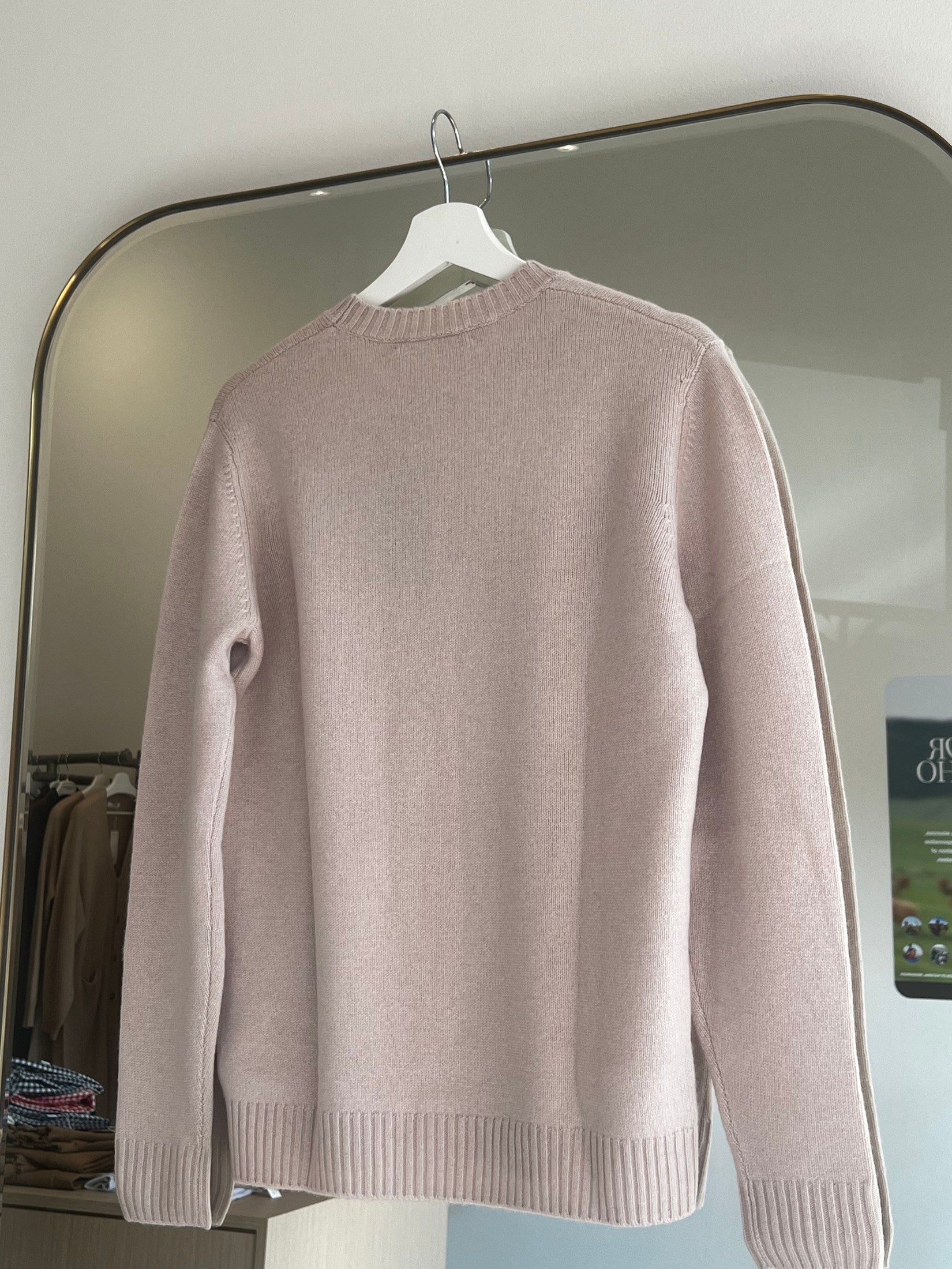 Soft pink round neck cashmere sweater hanging on white hanger with ribbed cuffs and hem visible from back