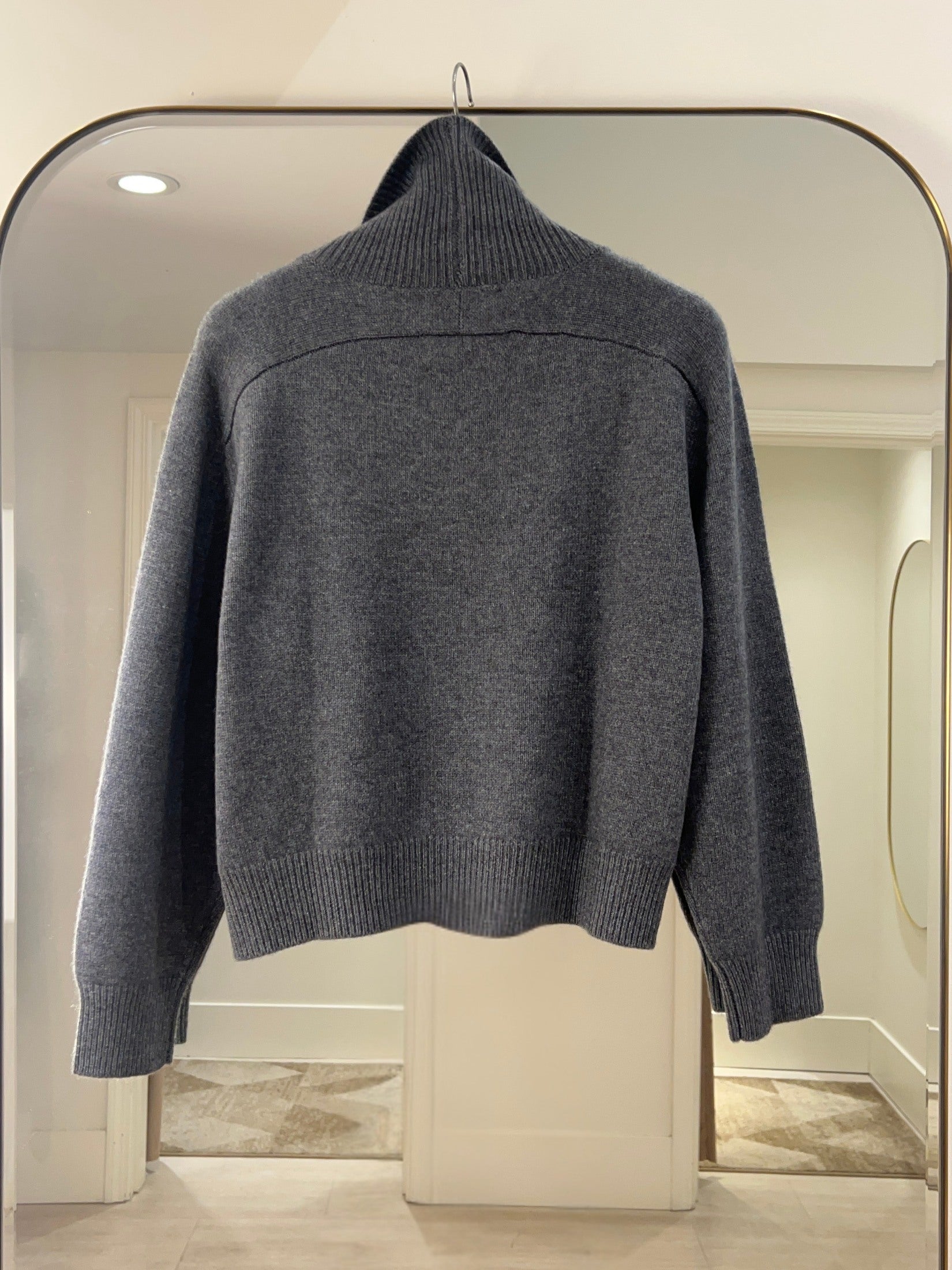 Dark gray turtle neck cashmere sweater with raglan shoulders hanging on a mirror in a bright room.