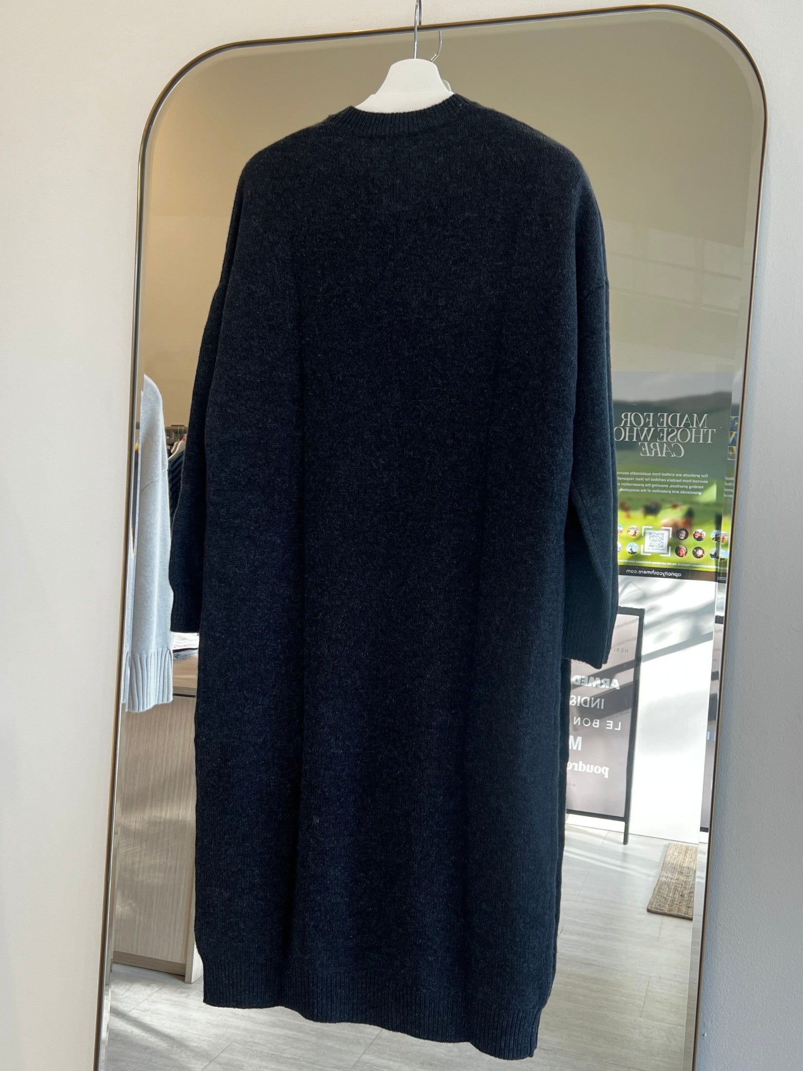 Back view of a black loose fit cashmere dress hanging on a white hanger in front of a mirror