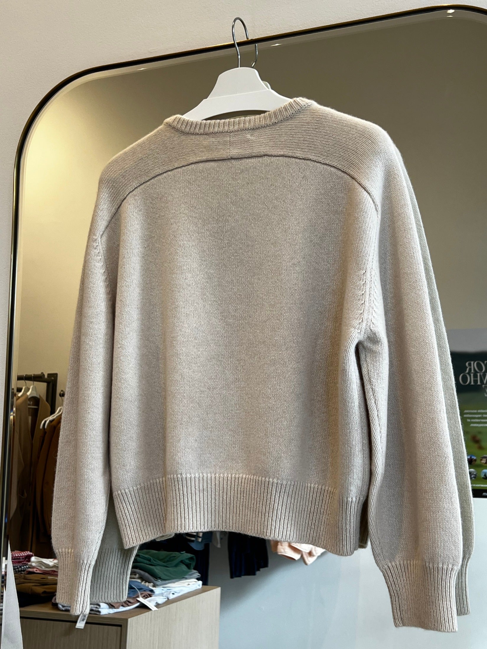 Beige round neck cropped cashmere sweater with raglan sleeves hanging on white hanger in store setting