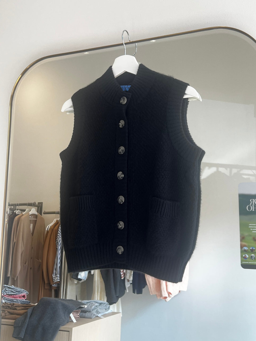 Black moss stitch cashmere button vest with two front pockets hanging on white hanger against mirror background