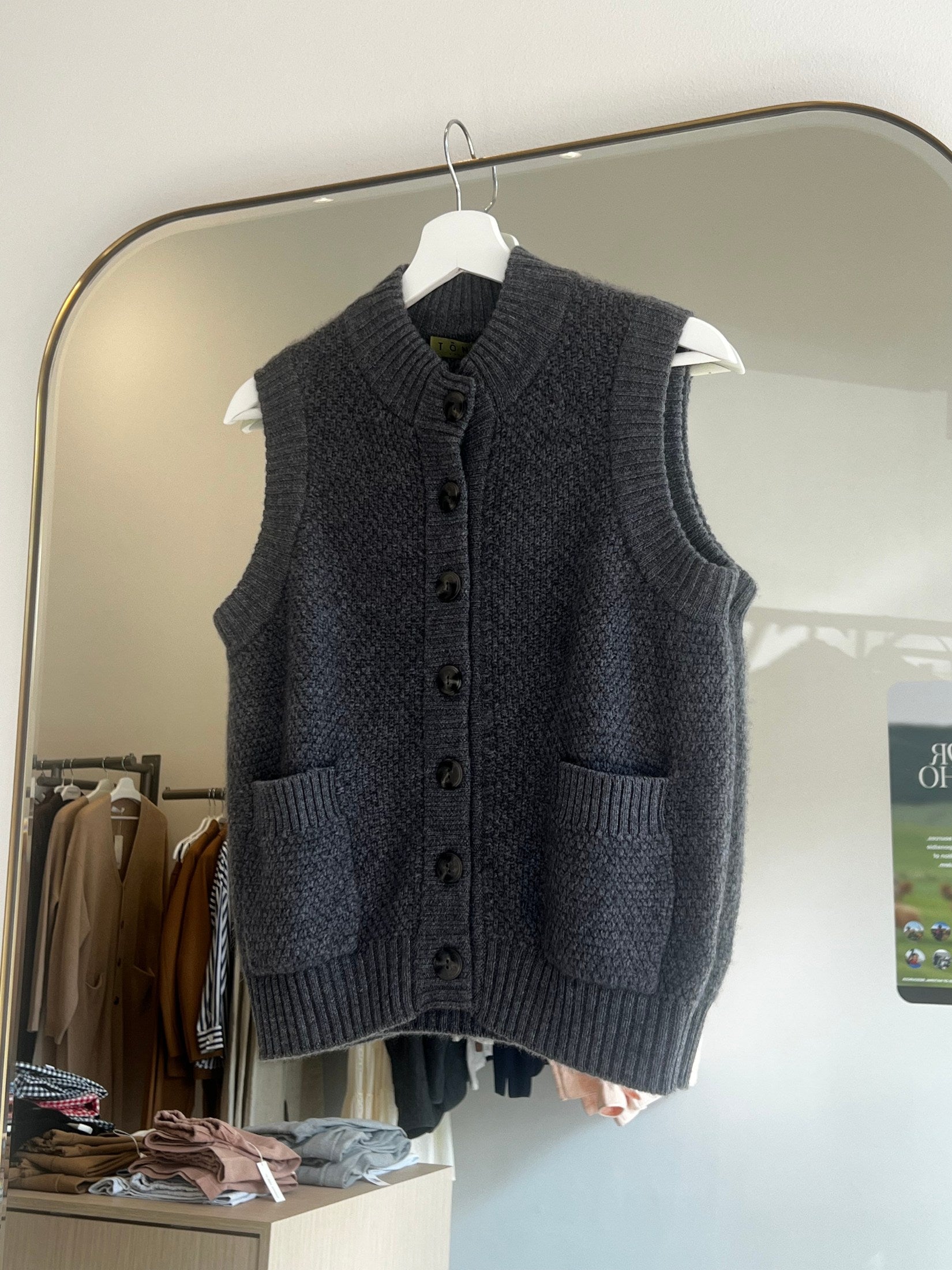 Dark gray Moss stitch cashmere button vest with two front pockets hanging on white hanger in modern room