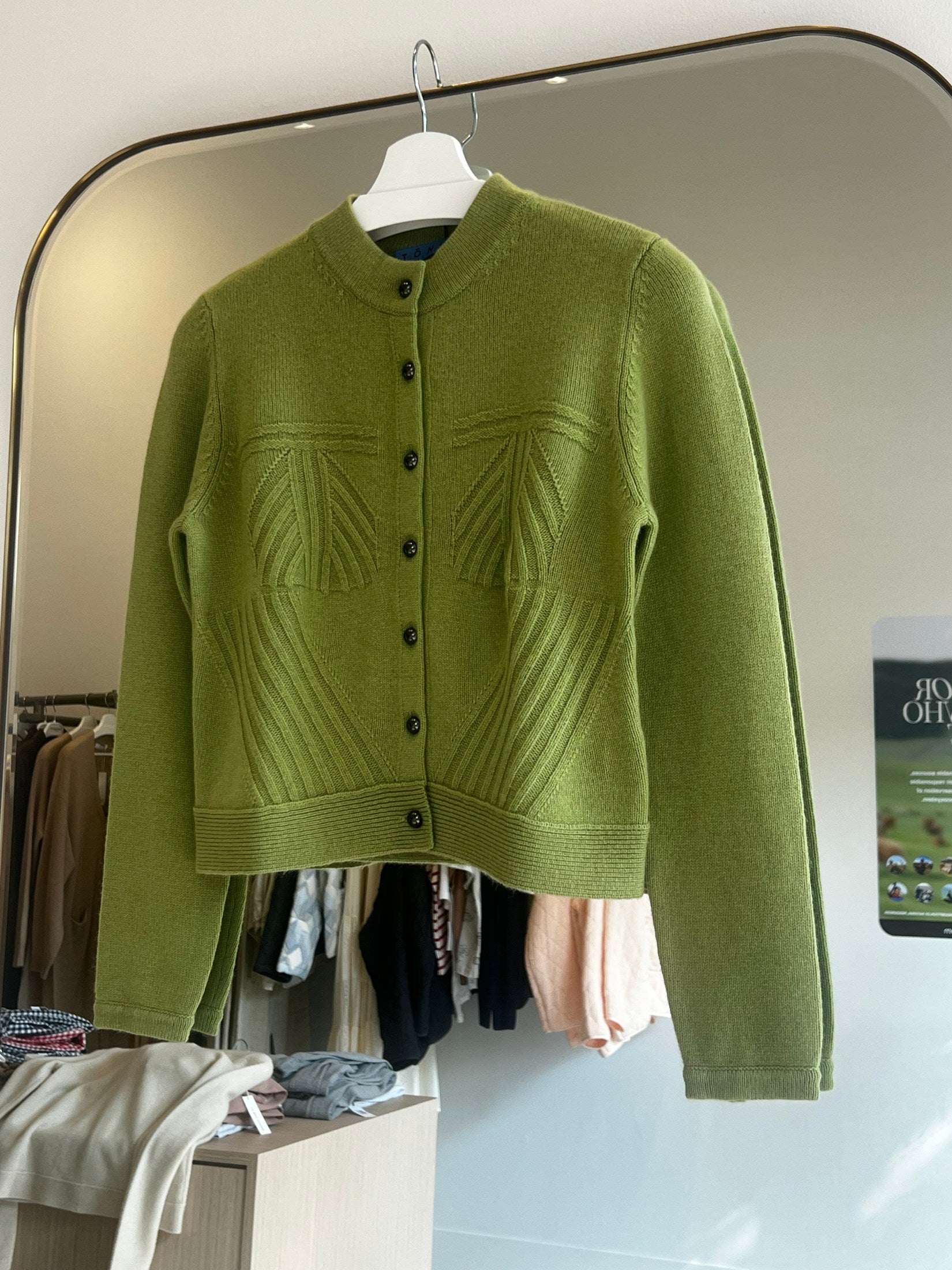 Green crop-length cashmere cardigan with button front and textured stitch details hanging on a white hanger.
